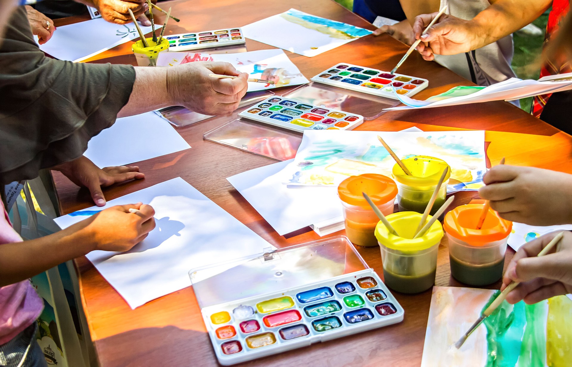 Diverse persone disegnano su carta usando colori ad acquerello seduti allo stesso tavolo. Masterclass di disegno.